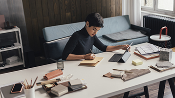 Focused professional working at a large desk with fabric samples, notebooks, and a tablet in a modern, softly lit studio.